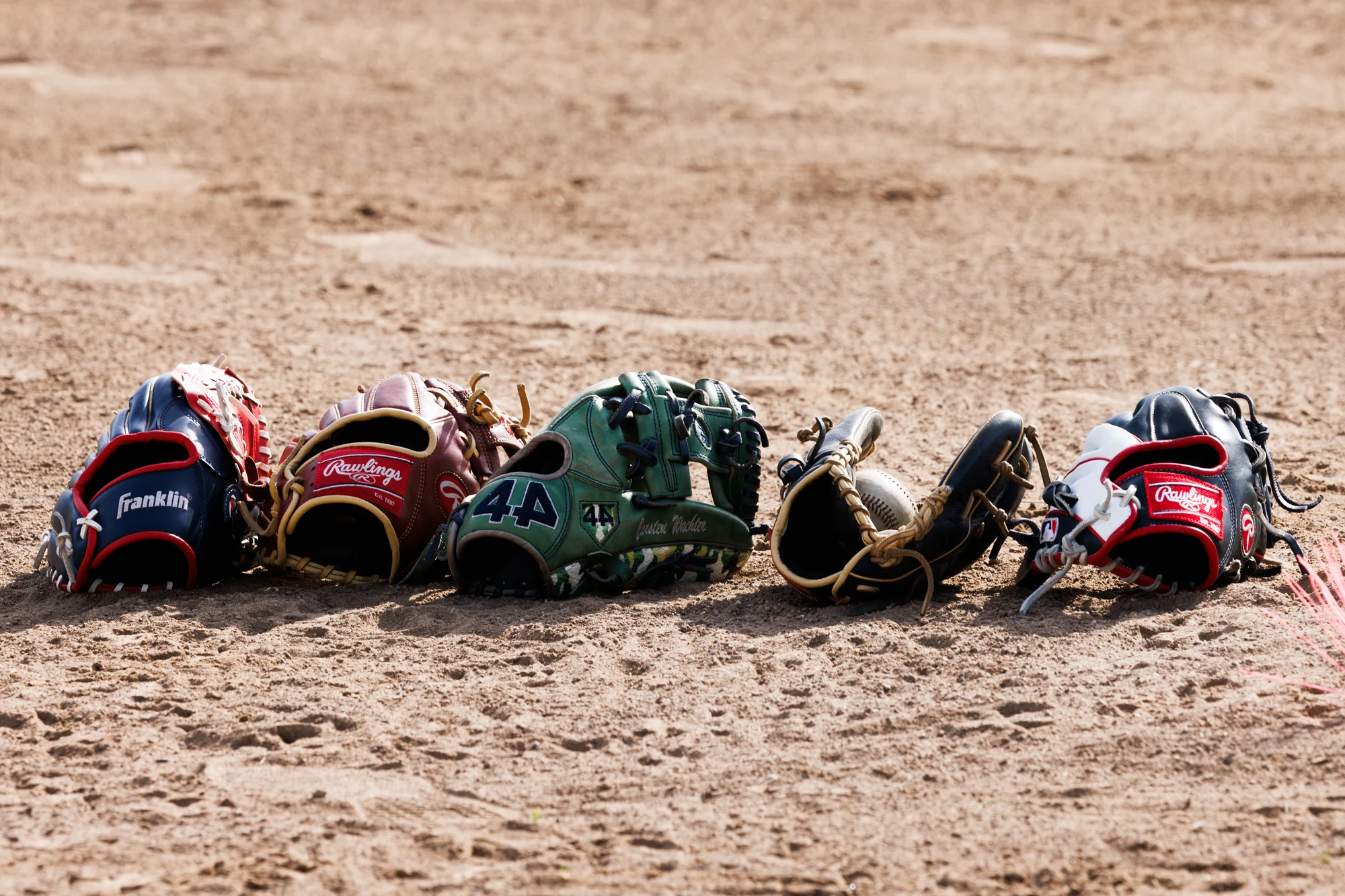 A row of well-used baseball gloves lined up on the infield dirt.