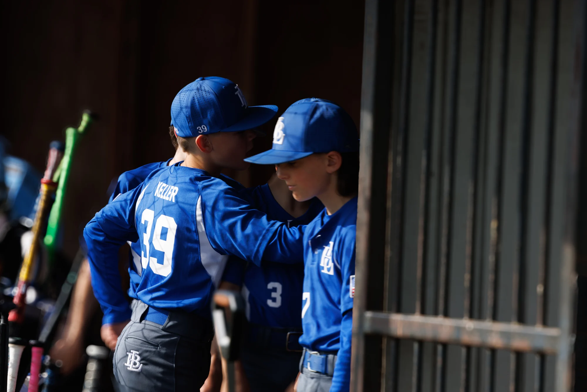 Two youth baseball teammates sharing a quiet moment in the dugout doorway.