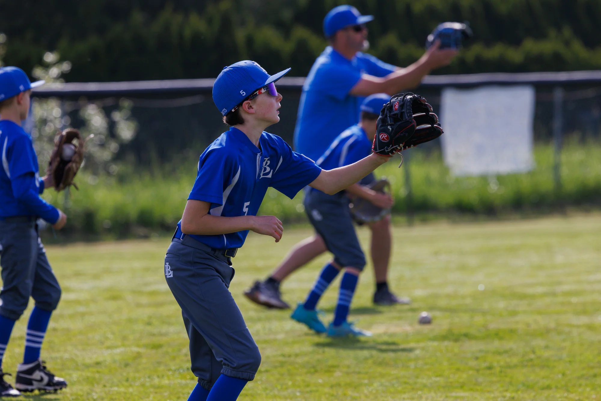 Youth baseball player reaching upward with a glove as teammates practice behind him.