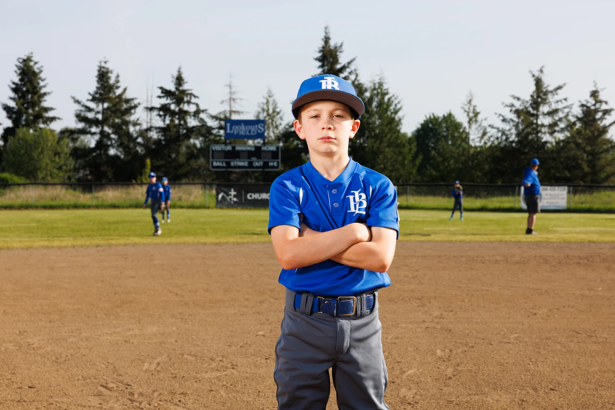 Youth baseball player standing on the infield with arms crossed for a team portrait.