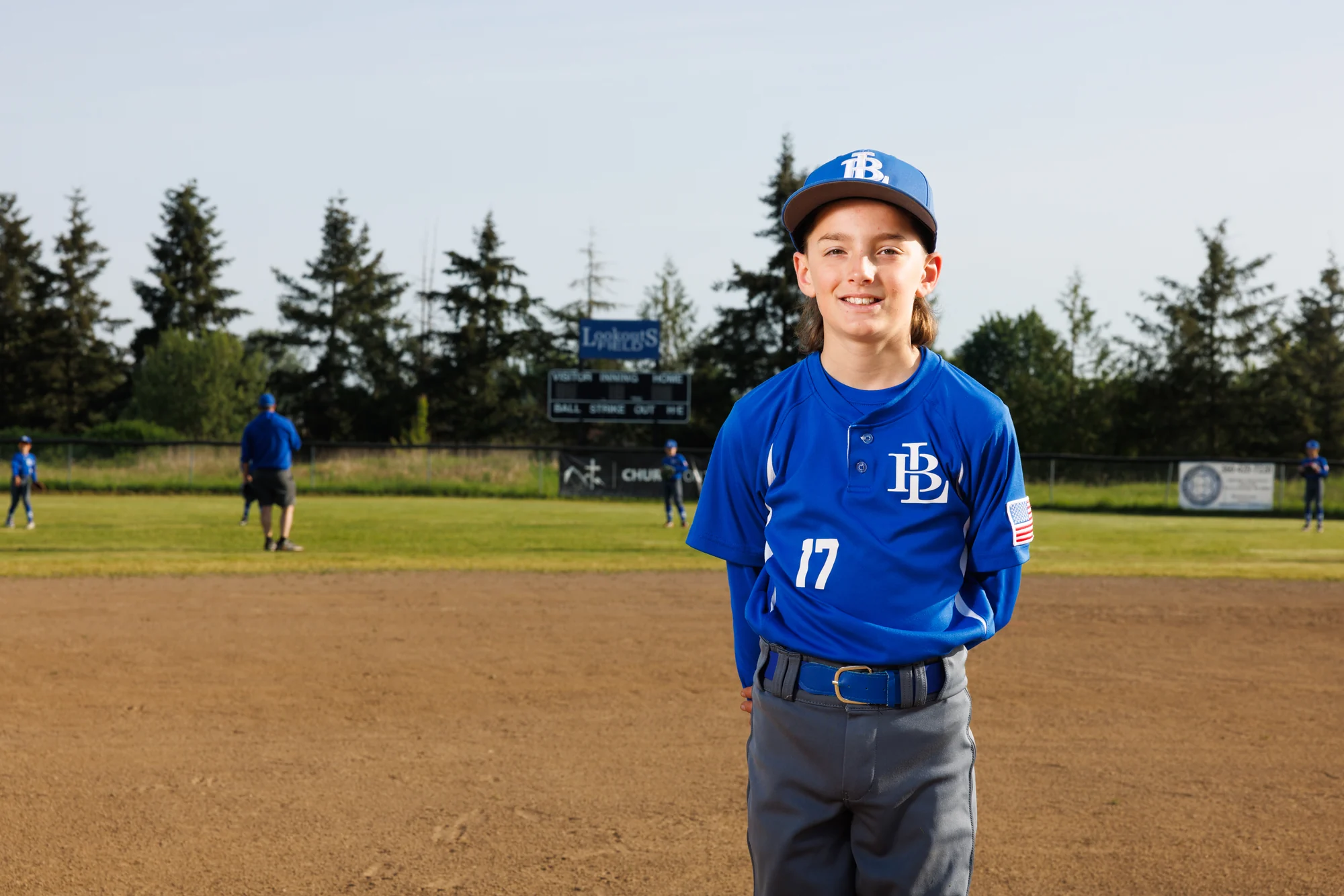 Smiling youth baseball player photographed on the infield in team uniform.