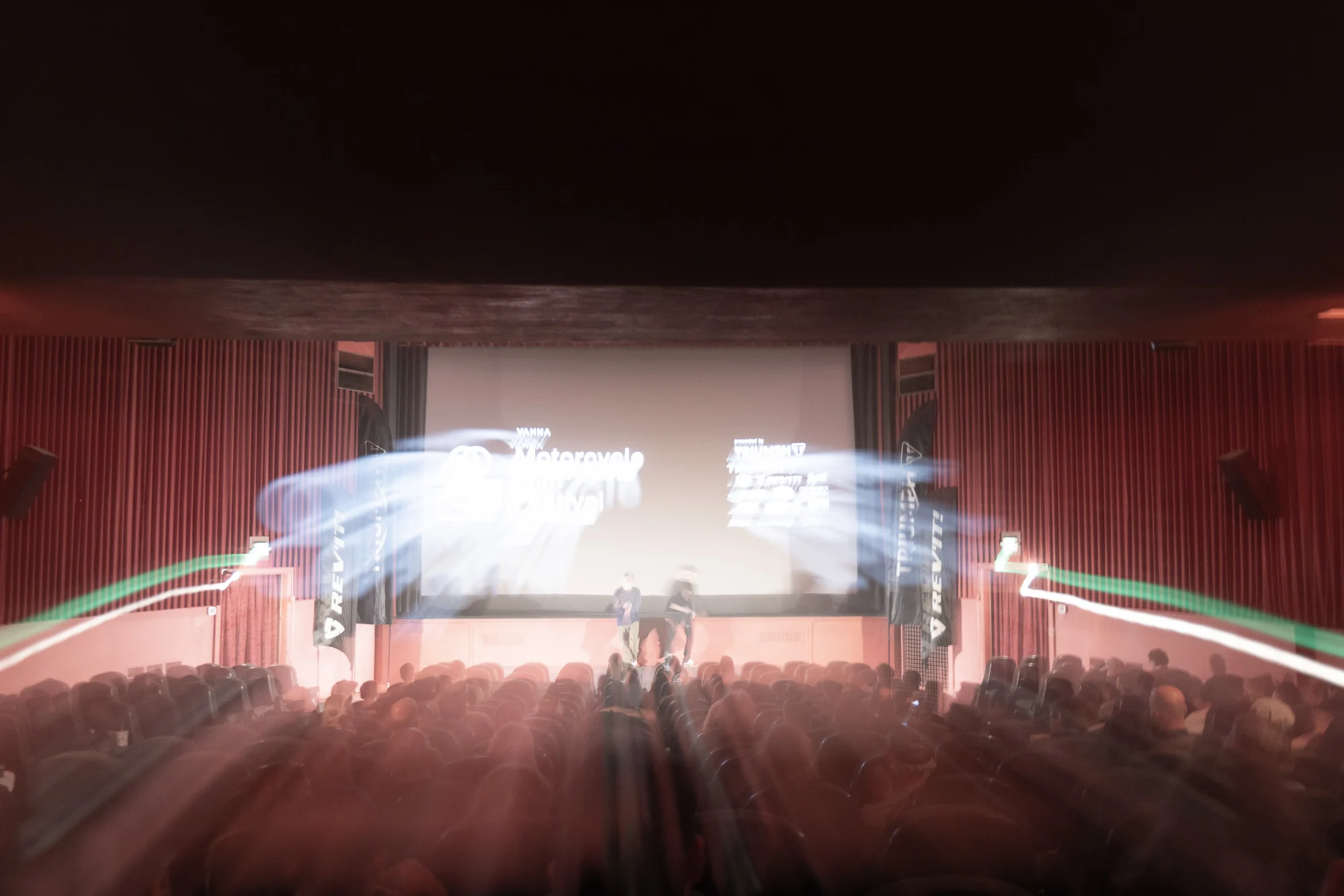 Long-exposure view across the festival audience toward the illuminated theater stage.