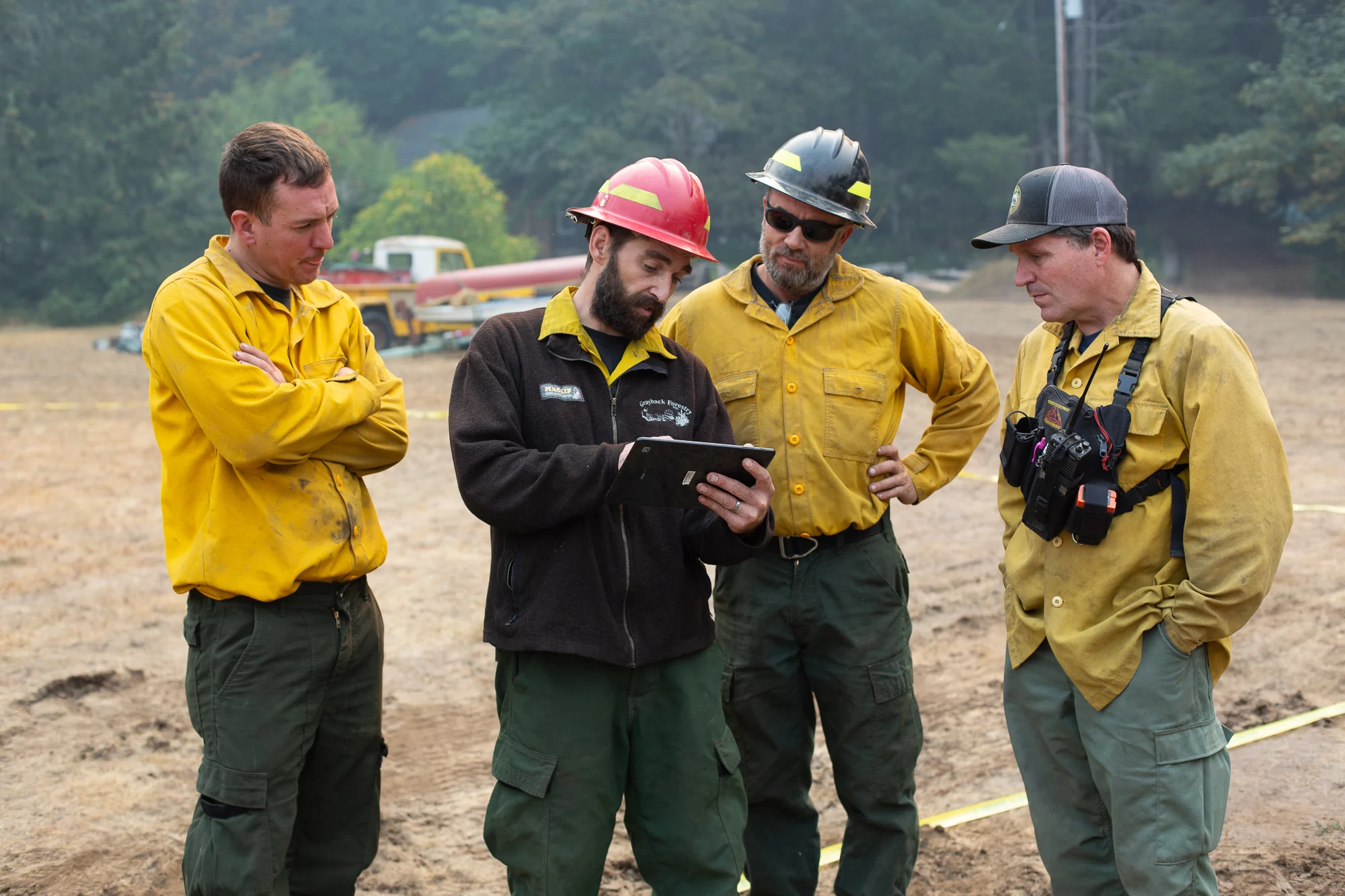 Four wildland firefighters reviewing operational information together on a tablet in the field.