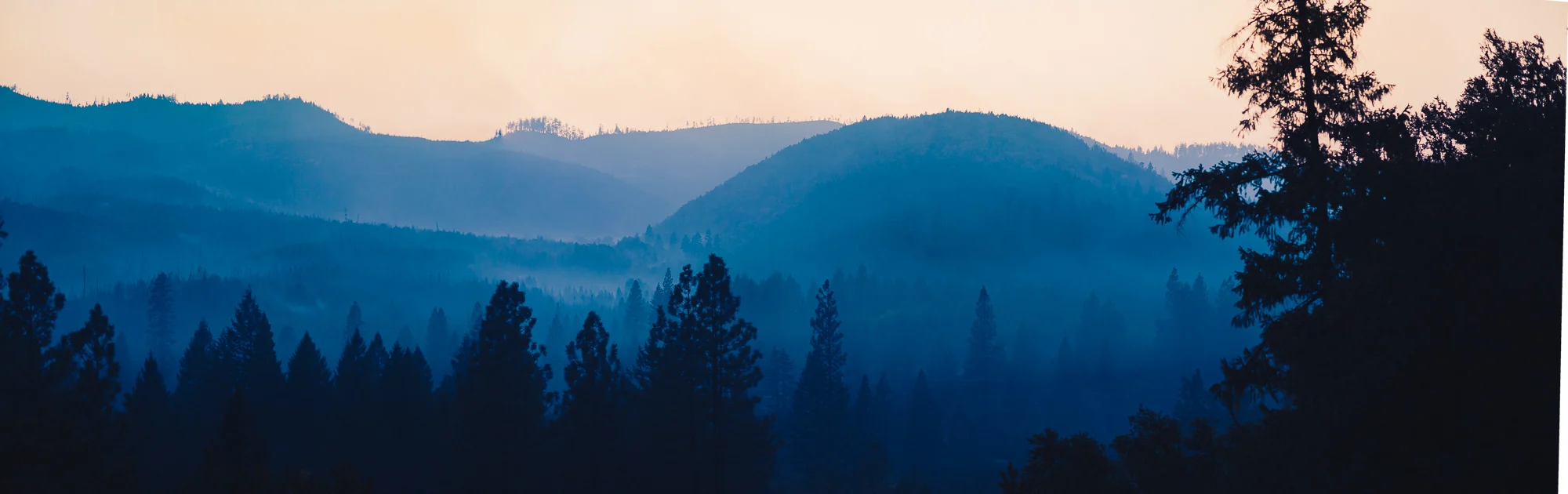 Layers of forested ridges receding beneath wildfire smoke at twilight.