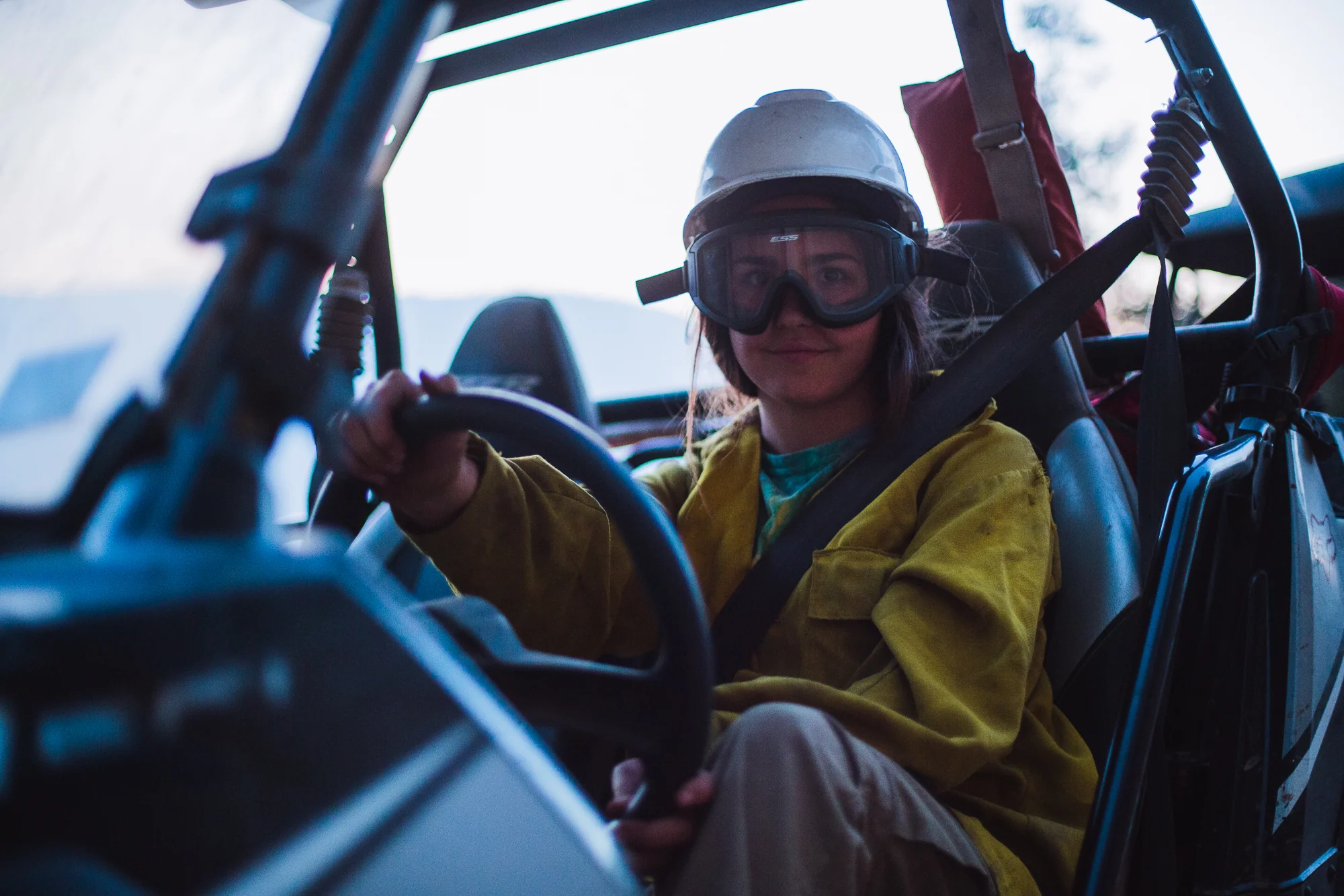 Wildland firefighter wearing a helmet and goggles while seated at the controls of an off-road vehicle.